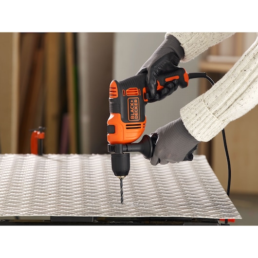 BLACK+DECKER BEH550 corded drill used on metal sheet, side angle, black and orange design.