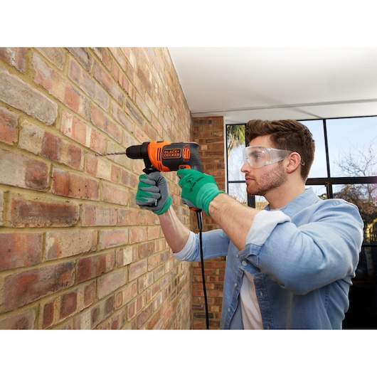 BLACKDECKER BEH550 corded drill used on brick wall, person wearing green gloves and blue shirt.