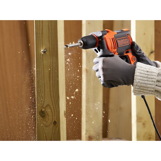 BLACKDECKER BEH710SA32 corded drill in use drilling into wooden beam, wood shavings flying, close-up.