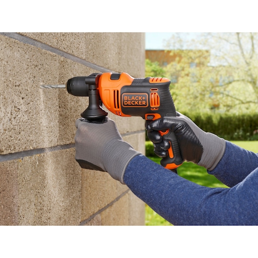 BLACK+DECKER BEH710SA32 hammer drill in use, drilling into exterior brick wall, operator wearing gloves.