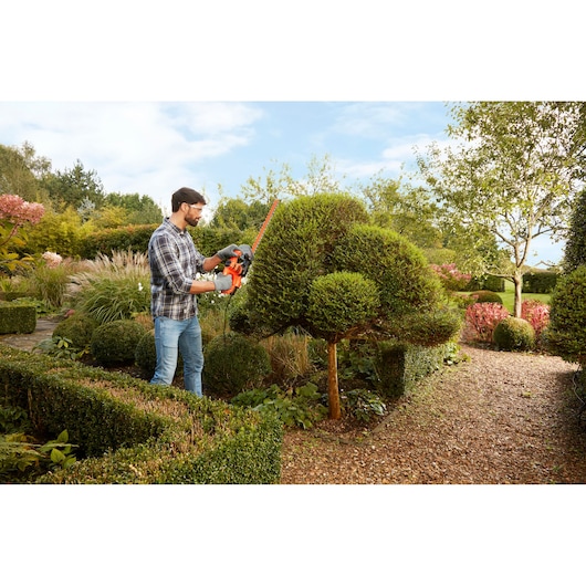 BLACKDECKER hedge trimmer BEHT201 used outdoors to trim decorative bushes in a garden.