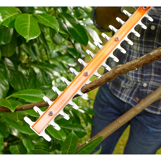BLACKDECKER BEHT201 hedge trimmer cutting a thick branch in a garden, close-up view.