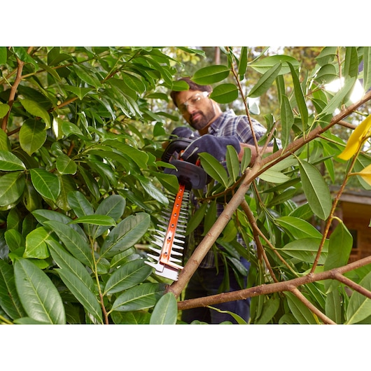 BLACKDECKER BEHTS401 hedge trimmer cutting thick branches in dense green foliage, outdoor setting.