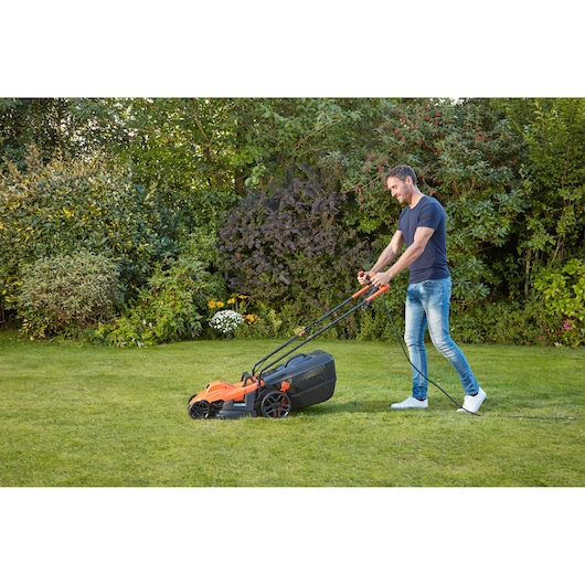 BLACKDECKER BEMW461BGL2 lawn mower in use on grass lawn, orange and black design, garden setting