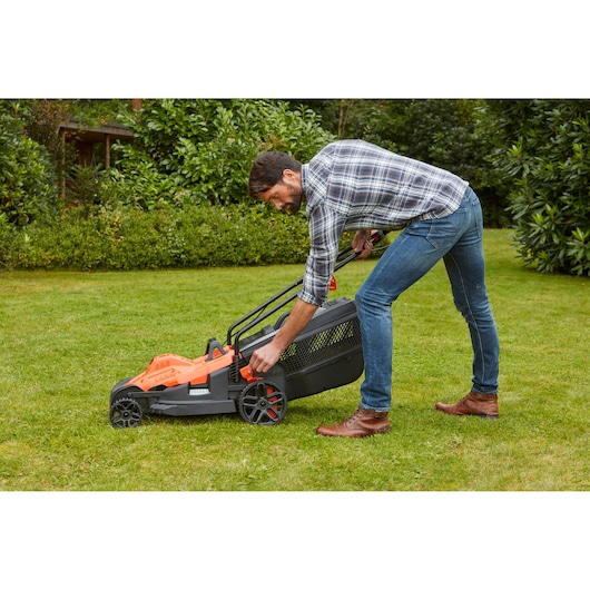 BLACKDECKER BEMW471BH lawn mower with grass bag in use on garden lawn.