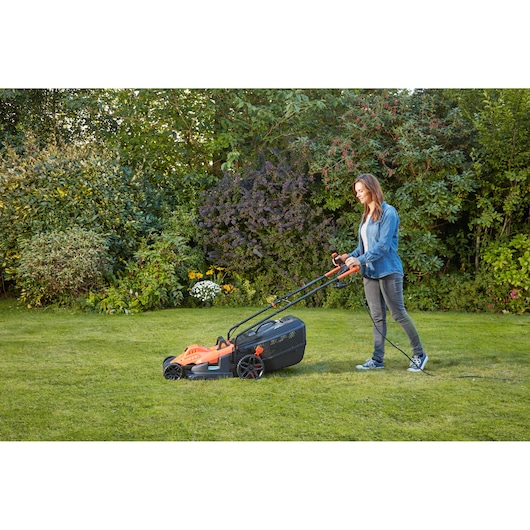 BLACKDECKER BEMW481BGL2 lawn mower in use outdoors on grass, showing orange and black design.