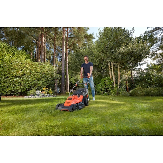 BLACKDECKER BEMW481BGL2 lawn mower in use on grass, orange and black design, outdoor garden setting.