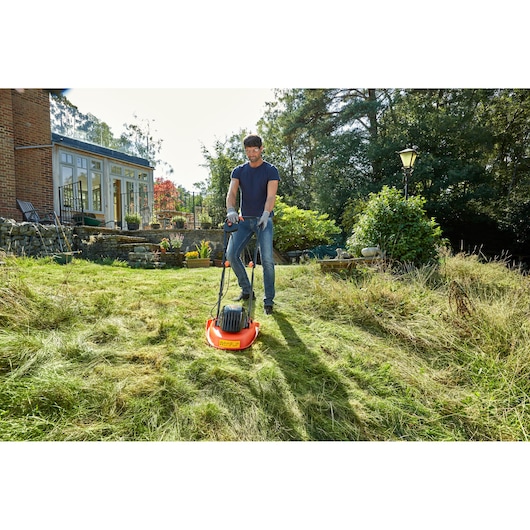 BLACKDECKER BEMWH551 lawn mower in use on grassy yard near house, orange body and black handle.