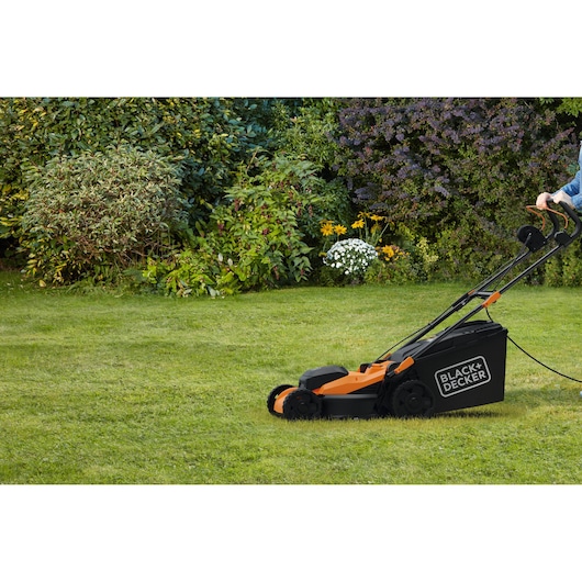 BLACK+DECKER BEMWP400-QS electric lawn mower in use on grass with garden plants in background.