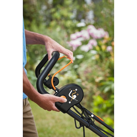 Close-up photo of BLACKDECKER BEMWP400-QS lawn mower handle with controls, orange accents, outdoors.
