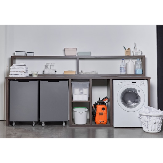 Photo of BLACKDECKER BEPW1300 pressure washer in orange color, placed in a laundry room shelf beside washing machine.