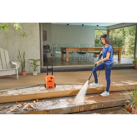 Photo of BLACKDECKER BEPW1650 pressure washer cleaning outdoor wooden deck, orange unit with hose and spray wand.