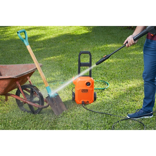Photo of BLACKDECKER BEPW1650 pressure washer cleaning a shovel beside a wheelbarrow on a lawn.