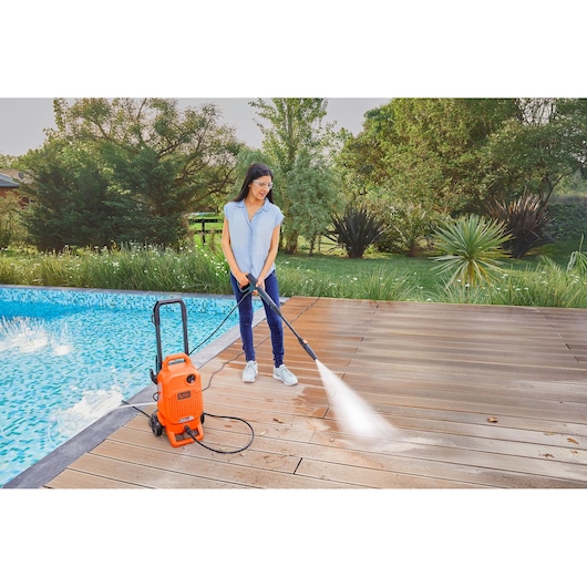 BLACKDECKER BEPW1700 pressure washer cleaning poolside wooden deck outdoors.