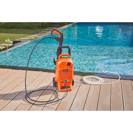 BLACK+DECKER BEPW1700 pressure washer with hose, orange, shown on poolside wooden deck.