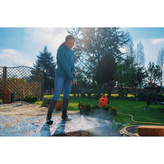 Photo of BLACKDECKER BEPW1700 pressure washer used outdoors to clean a stone patio, bright orange unit visible.