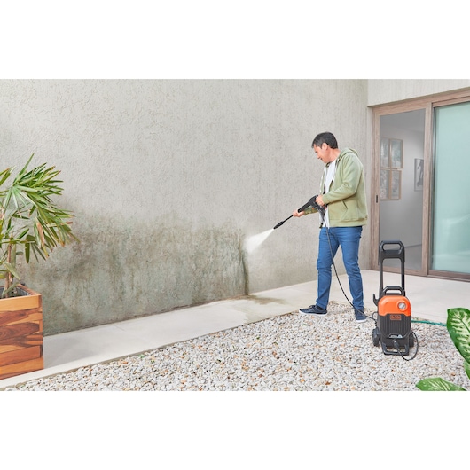 Photo of BLACKDECKER BEPW2000 pressure washer cleaning an outdoor wall, with orange and black unit on stone patio.