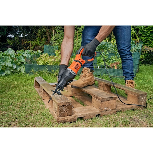 Photo of BLACK+DECKER BES301 reciprocating saw cutting wooden pallet outdoors, operator wearing gloves and boots.