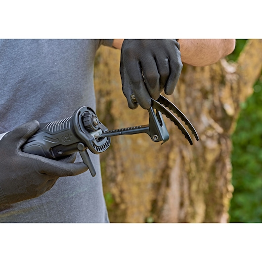 Photo of BLACKDECKER BES301 saw being held by a person wearing black gloves outdoors, with tree and greenery in background.
