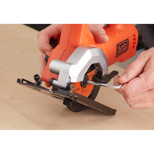 Photo of BLACK+DECKER BES510 compact circular saw, close-up of blade adjustment with wrench on wooden surface.