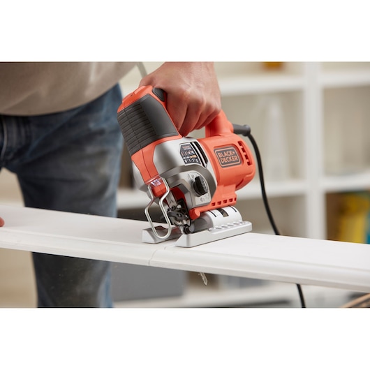 Photo of BLACKDECKER BES610K jigsaw cutting wood, close-up view showing orange and black housing.