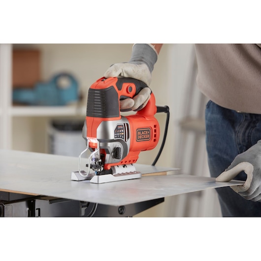 Photo of BLACK+DECKER BES610K jigsaw in use, cutting a metal sheet, operator wearing gloves.