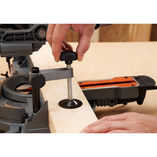 BLACKDECKER BES702 miter saw in use, wood clamped securely with adjustable hold-down clamp, side angle.