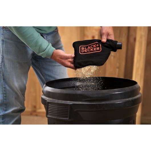 Photo of person emptying dust from BLACK+DECKER BES702 dust bag into a black trash bin.