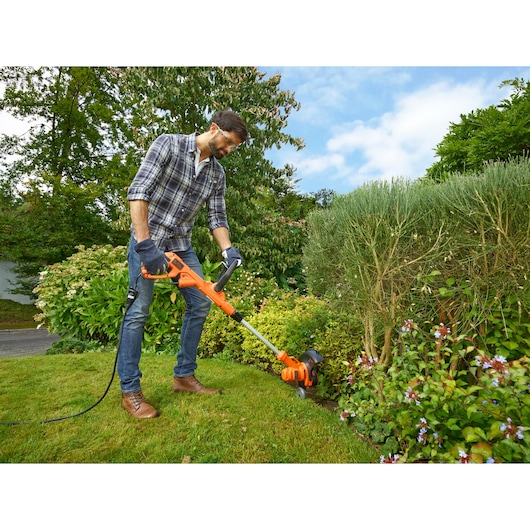Photo of BLACKDECKER BESTA530C10 electric grass trimmer in use, orange body, cutting lawn edges outdoors.