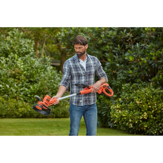 Photo of BLACKDECKER BESTA530C10 orange electric string trimmer held outdoors in garden.