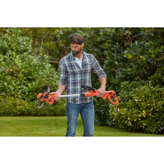 BLACKDECKER BESTA530C10 orange string trimmer held outdoors by a person, garden background.