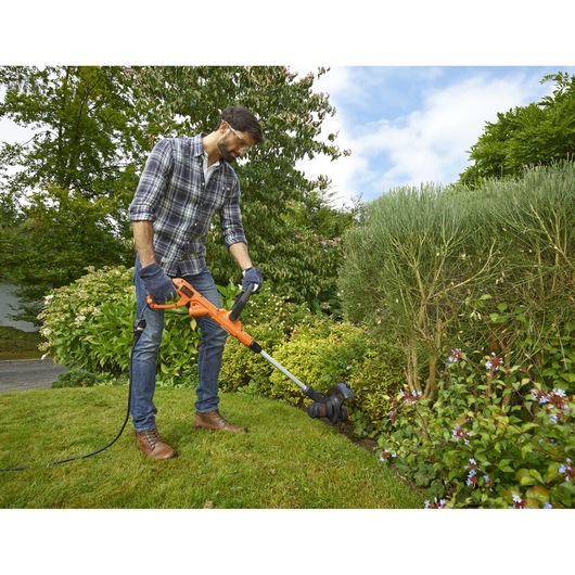 BLACKDECKER BESTE625 grass trimmer used in a garden setting with greenery and flower beds.