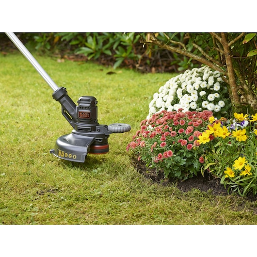 BLACKDECKER BESTE630 grass trimmer in use near colorful flower bed, garden setting.