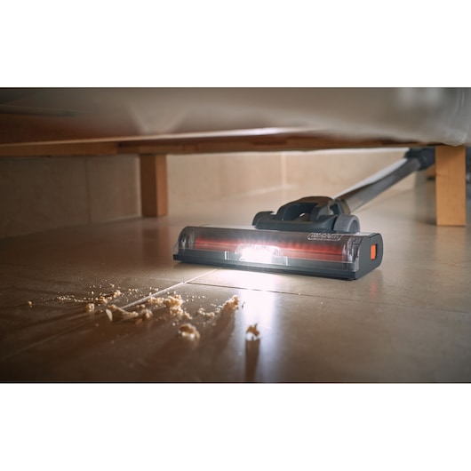 BLACKDECKER BHFEA18D1 vacuum cleaner head with LED light cleaning debris from tile floor under furniture.