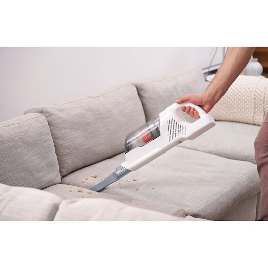 BLACKDECKER BHFEA515J handheld vacuum cleaning crumbs from a light grey sofa, angled view.