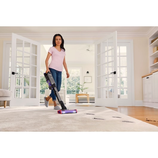 BLACKDECKER BHFEA640WP cordless stick vacuum in use on living room carpet with visible dirt.
