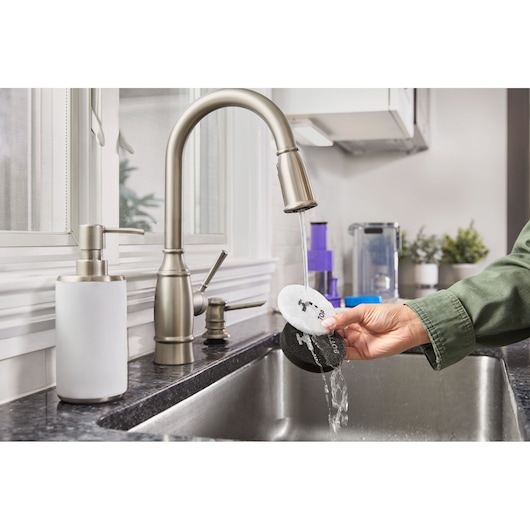Photo of a hand rinsing BLACKDECKER BHFEA640WP cleaning pads under a kitchen faucet in a modern sink.