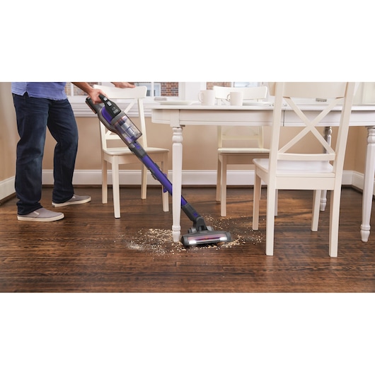 Photo of BLACKDECKER BHFEV182CP cordless stick vacuum cleaning debris from wooden floor near dining table.