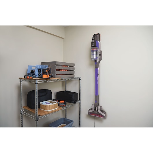 BLACKDECKER BHFEV182CP cordless stick vacuum mounted on wall in storage room beside metal shelf with tools.