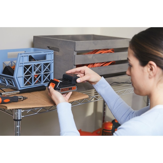 BLACKDECKER BHFEV182C lithium 18V battery held by person in workshop setting, visible storage boxes.