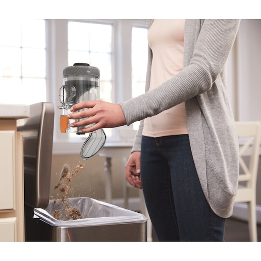BLACKDECKER BHFEV182C vacuum dustbin being emptied into a kitchen trash can, side view.