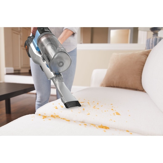 BLACKDECKER BHFEV362D handheld vacuum cleaning crumbs from a white sofa in a living room.