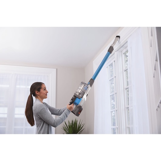 BLACKDECKER BHFEV362D cordless stick vacuum with extension cleaning high window trim indoors.