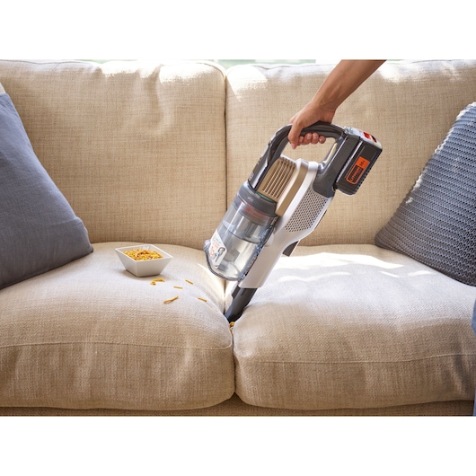 Photo of BLACK+DECKER BHFEV36B2D cordless vacuum cleaner being used to clean crumbs from a beige sofa.