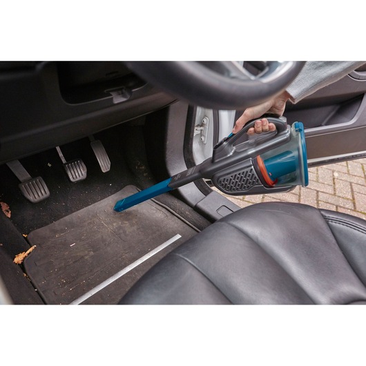 BLACKDECKER BHHV320J handheld vacuum cleaning car floor with blue nozzle attachment.