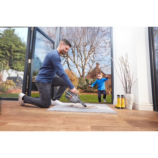BLACKDECKER BHHV520JF handheld vacuum photo in use cleaning a rug in a modern home with open doors to garden.