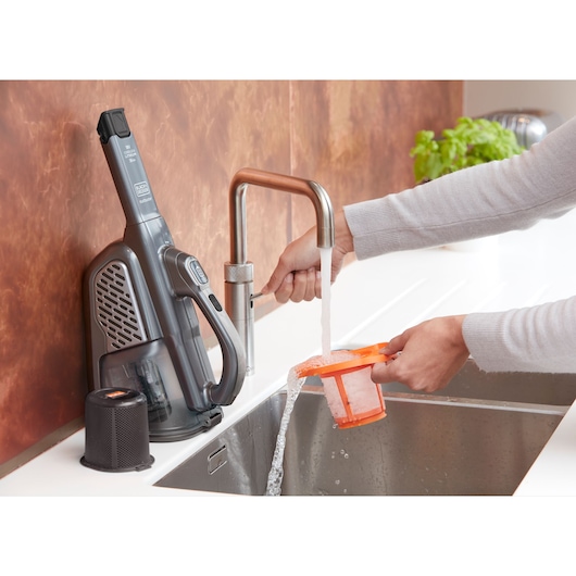 BLACK+DECKER BHHV520JF handheld vacuum filter being cleaned under running water in a kitchen sink.