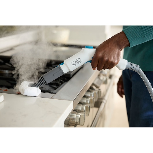BLACK+DECKER BHSMP2008 handheld steam cleaner used to clean a stovetop, producing visible steam.