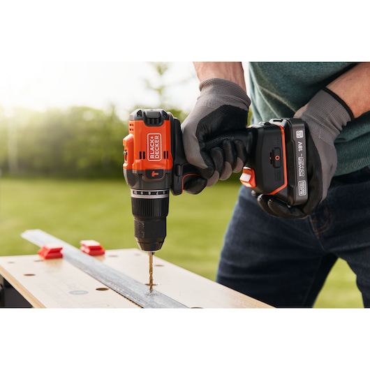 Photo of BLACKDECKER BLD683D1 cordless drill in use, drilling metal on a workbench outdoors.