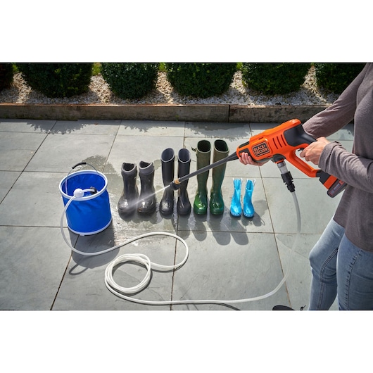 Photo of BLACK+DECKER portable washer BZOB1 cleaning rubber boots outdoors with hose and blue bucket.